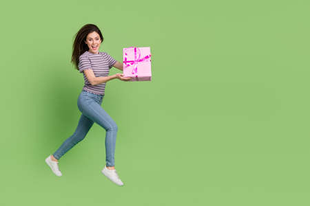 Full length body size view of attractive cheerful thin girl jumping carrying giftbox isolated on...