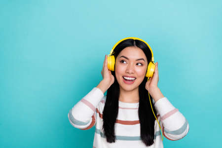 Photo of impressed young lady listen music look promo wear headphones white pullover isolated on turquoise color backgroundの写真素材