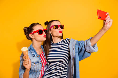 Portrait of two charming nice ladies make selfie eat ice cream kiss lips isolated on yellow color...