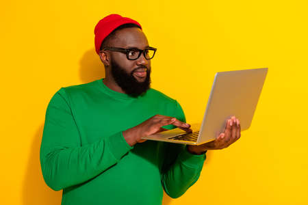 Portrait of attractive focused skilled guy using laptop typing finance project isolated over bright yellow color backgroundの写真素材
