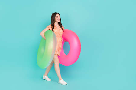 Photo of pretty sweet lady dressed orange clothes walking holding two swimming circles empty space...