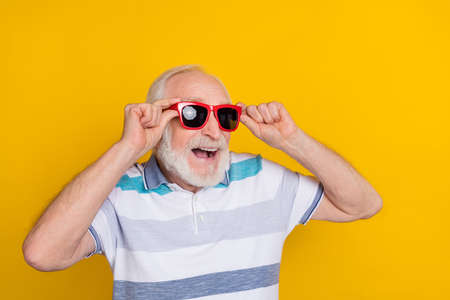 Portrait of attractive funny dreamy cheerful grey haired man touching specs having fun isolated over bright yellow color backgroundの写真素材