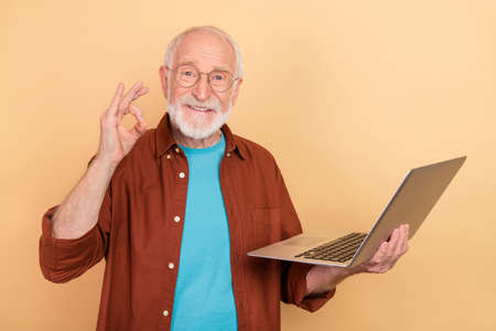 Photo of pretty funny guy pensioner dressed brown shirt rising working modern device okey sign...