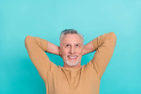 Portrait of cheerful minded man hands behind head look interested up empty space isolated on teal color backgroundの写真素材