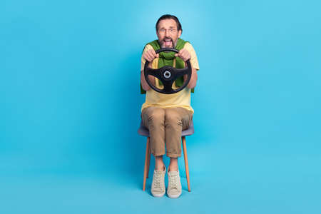 Full length photo of impressed terrified person sit chair hold wheel open mouth isolated on blue...
