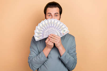 Photo of young man wealthy cover face money profit benefit salary isolated over beige color backgroundの写真素材