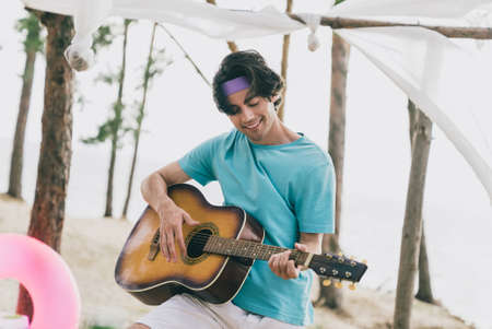 Portrait of attractive cheerful guy playing guitar spending day weekend relax enjoying good weather at beach picnic outdoorsの写真素材