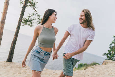 Photo of adorable pretty two people together holding arms enjoying good weather walking outside ocean waterの写真素材