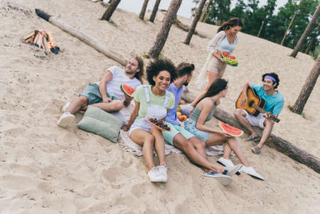 Photo of funny cute young buddies dressed casual outfits enjoying tasty fruits listening songs outdoors countrysideの写真素材