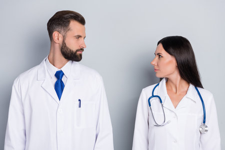 Profile portrait of two confident serious doctors look each other isolated on grey color backgroundの写真素材