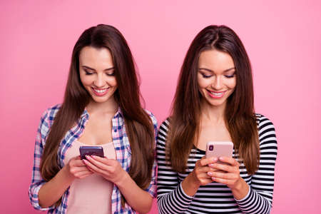 Photo of two pretty cheerful ladies hold use telephone write typing post comment isolated on pink color backgroundの写真素材