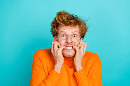 Photo of scared afraid guy dressed orange sweater eyewear biting fingers isolated turquoise color...