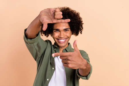 Portrait of attractive cheerful wavy-haired guy showing photo frame posing taking selfie isolated over beige pastel color backgroundの写真素材