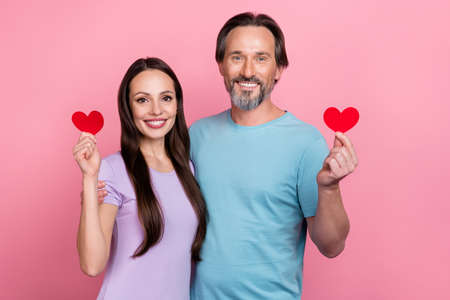 Portrait of positive partners hold show small red paper heart symbol isolated on pink color backgroundの写真素材