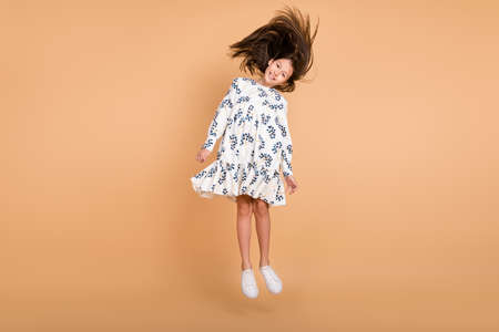 Full length body size view of attractive cheerful girl jumping throwing hair isolated on beige...