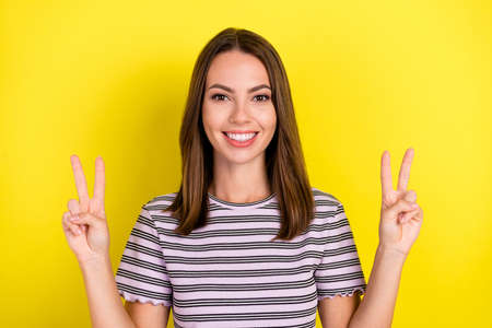 Photo of cool young brunette lady show v-sign wear striped t-shirt isolated on yellow background