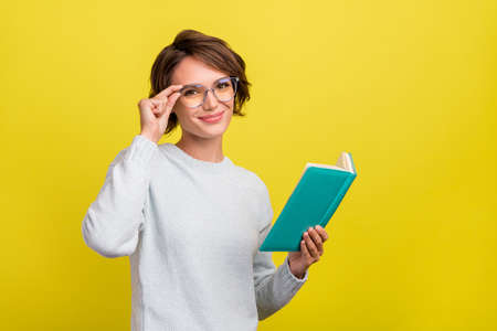 Photo of cute millennial brunette lady read book wear eyeweear blue sweater isolated on yellow color...