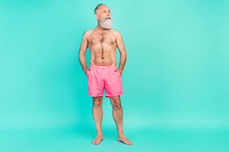 Photo of minded muscular old man hands pockets look empty space wear pink shorts isolated teal color...