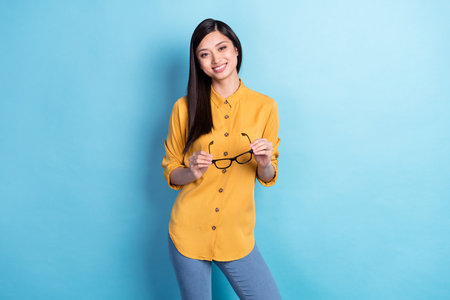 Photo of young attractive asian business woman happy positive smile hold eyeglasses isolated over blue color backgroundの写真素材