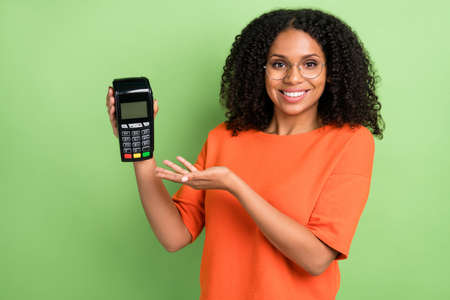 Photo of young african woman happy positive smile show terminal nfc payment isolated over green...