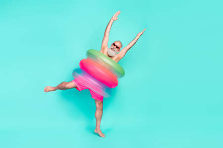 Photo of crazy clubber old man dance raise hands wear pile lifebuoy sunglass shorts isolated teal color backgroundの写真素材