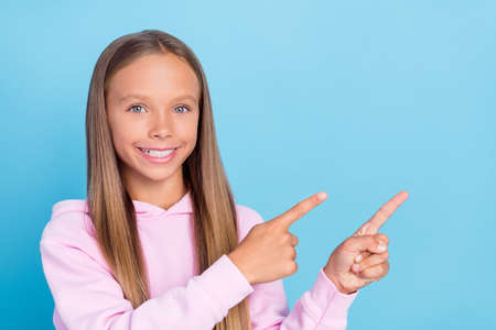 Photo of joyful happy young little girl point finger empty space news follow sale isolated on blue...