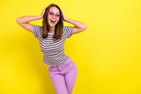 Photo of impressed young brunette lady hands head look empty space wear eyewear t-shirt isolated on yellow backgroundの写真素材