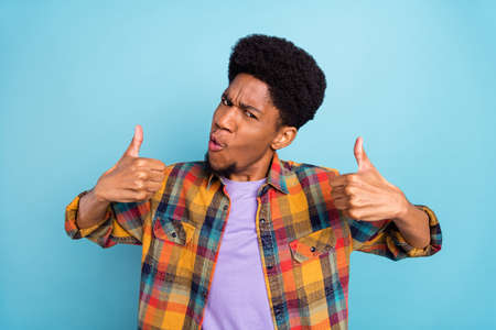 Photo of cool millennial brunet guy show thumb up wear yellow shirt isolated on blue color backgroundの写真素材