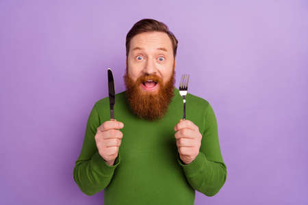Portrait of crazy positive man hold fork knife open mouth cant wait food isolated on purple color backgroundの写真素材