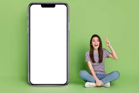 Portrait of beautiful cheerful girl sitting pointing up copy space news offer advert order isolated...