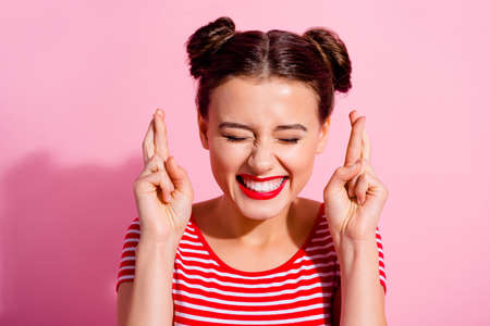 Photo of cheerful funky girl closed eyes crossed fingers toothy smile isolated on pink color...