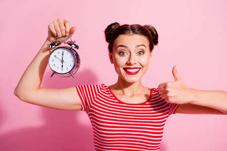 Portrait of cheerful nice girl hold classic clock hand finger show thumb up isolated on pink color backgroundの写真素材