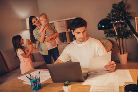 Photo of pretty funny mother little children busy father working modern device read documents late night indoors room home houseの写真素材