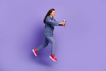 Full length profile photo of excited active person jump rush look empty space hold thermo cup isolated on violet color backgroundの写真素材