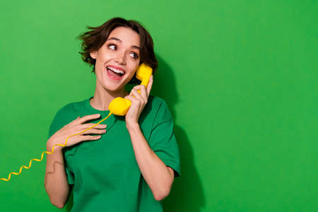 Photo of funny excited woman dressed summer t-shirt talking phone looking empty space isolated green color backgroundの写真素材