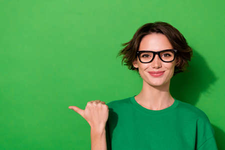 Photo of cute adorable woman wear casual t-shirt eyeglasses pointing thumb empty space isolated green color backgroundの写真素材