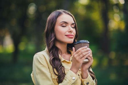 Portrait of attractive cheery calm peaceful long-haired girl enjoying drinking espresso in forest outdoorsの写真素材