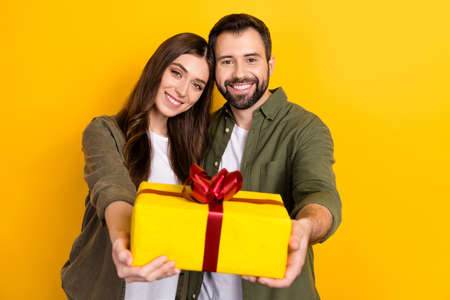 Photo of two idyllic positive people hold give you giftbox isolated on yellow color backgroundの写真素材
