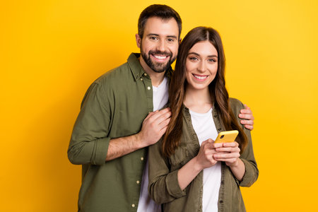 Portrait of attractive cheerful couple using device surfing web app 5g isolated over bright yellow color backgroundの写真素材