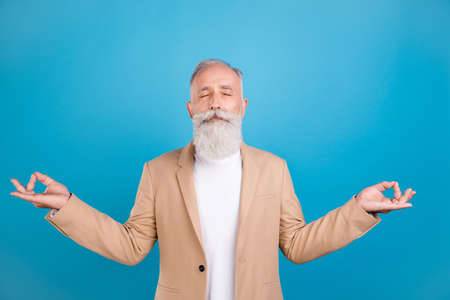 Portrait of handsome elegant dreamy grey-haired man meditating isolated over bright blue color...