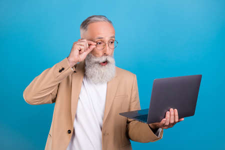Portrait of attractive amazed grey-haired man using laptop pout lips reading report isolated over...