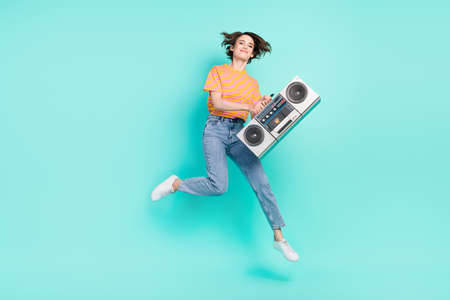 Photo of adorable funky young lady wear orange t-shirt jumping high holding boom box smiling isolated turquoise color backgroundの写真素材