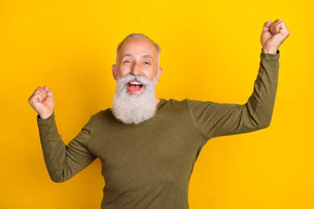 Photo of funky attractive mature man dressed khaki pullover rising fists smiling isolated yellow color backgroundの写真素材