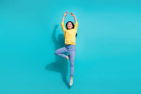 Full length photo of dreamy shiny woman wear yellow pullover dancing jumping high isolated teal color backgroundの写真素材