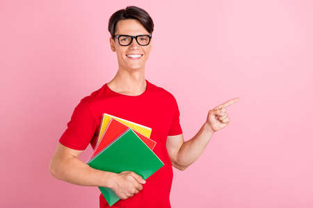 Photo of cute clever young man wear red t-shirt smiling pointing finger empty space isolated pink color backgroundの写真素材