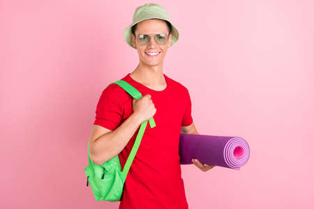 Photo of pretty funny young guy dressed red t-shirt headwear holding yoga mat smiling isolated pink color backgroundの写真素材