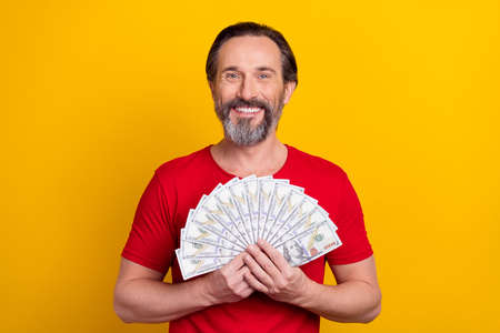 Photo of funky young brunet man hold money wear red t-shirt isolated on yellow color background
