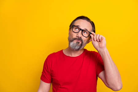 Photo of senior man hand touch eyeglasses look empty space thoughtful plan isolated over yellow...