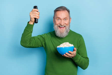 Photo of positive aged man raise remote control hold pop corn snack watch series comedy isolated...