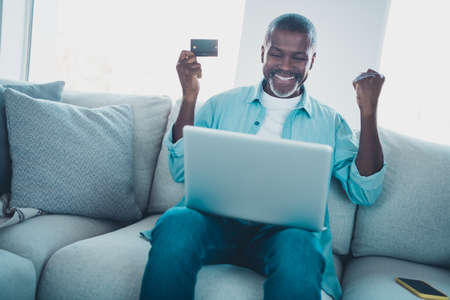 photo of excited aged man use deposit card netbook bet win fist up increase budget in modern house roomの写真素材